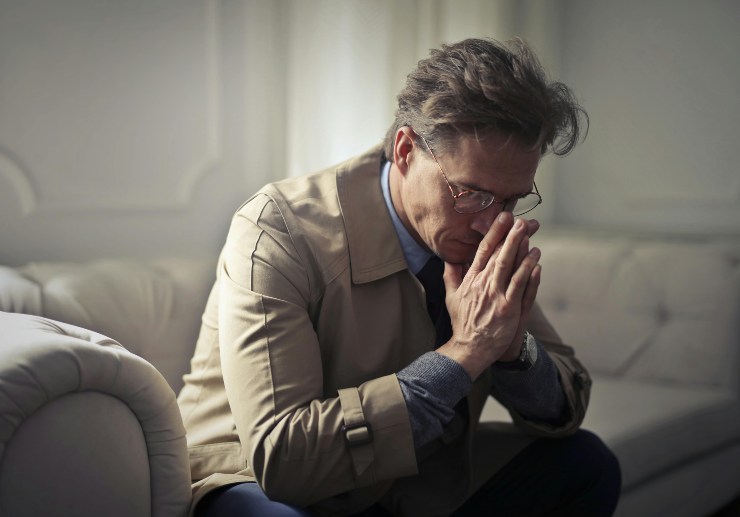 uomo seduto con le mani congiunte davanti al viso e l'espressione preoccupata