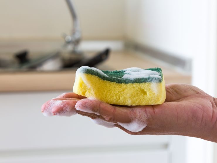 mano con spugna da cucina piena di schiuma