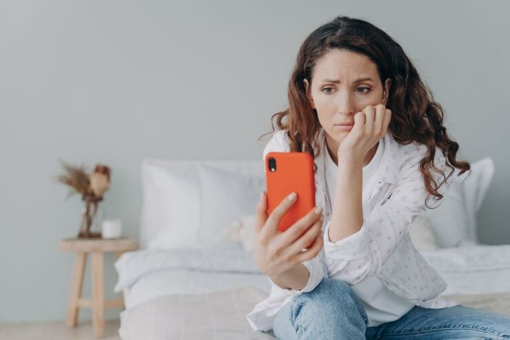 Ragazza seduta e pensierosa leggere qualcosa sul suo smartphone con cover arancione