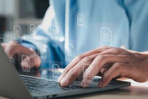 Uomo in camicia azzurra al PC con icone documento