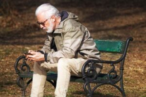 uomo anziano seduto su una panchina con un cellulare in mano
