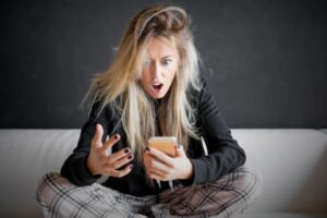 donna seduta con il cellulare in mano e la bocca aperta per lo shock
