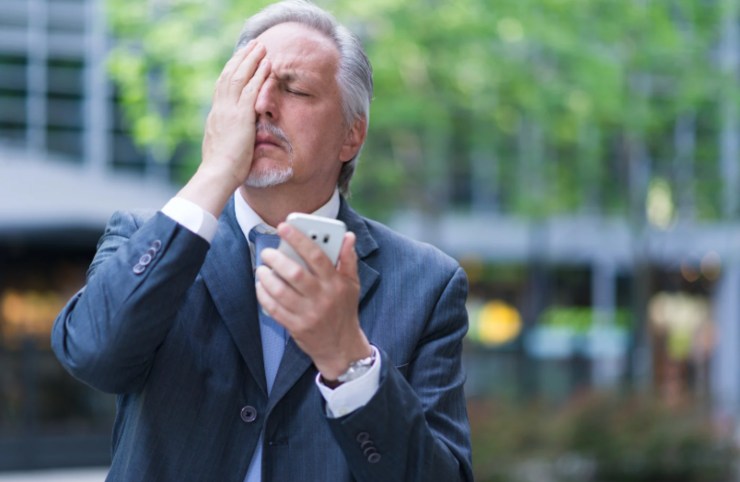 uomo disperato con una mano in faccia e il cellulare nell'altra mano