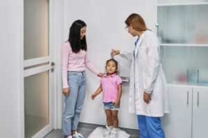 pediatra che misura la statura di una bambina con la mamma lì accanto