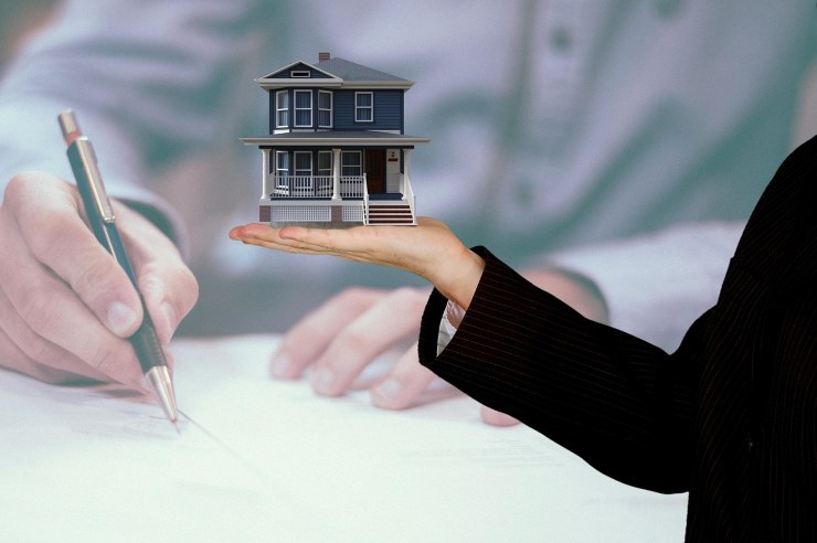 uomo che firma un contratto e donna con una casetta in miniatura in mano