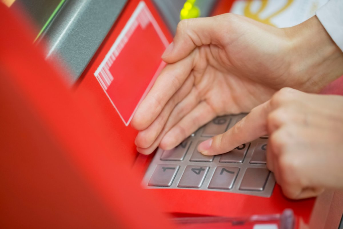 persona che digita il codice pin sulla tastiera dello sportello bancomat
