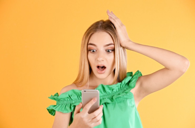 donna stupita con una mano sulla testa e nell'altra il cellulare