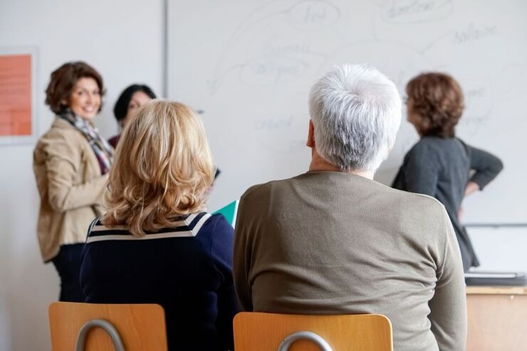 Due persone di spalle in un'aula con altre tre donne alla lavagna 