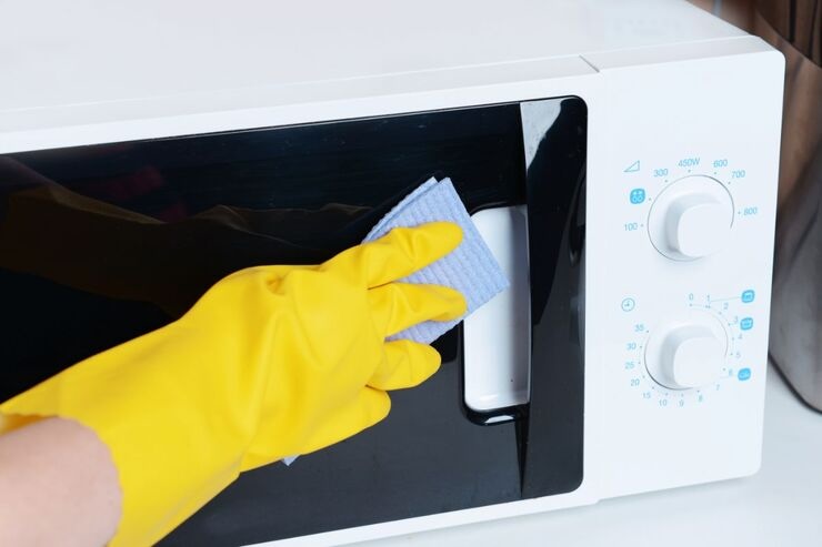 Mano con guanto giallo pulisce vetro microonde con straccio blu