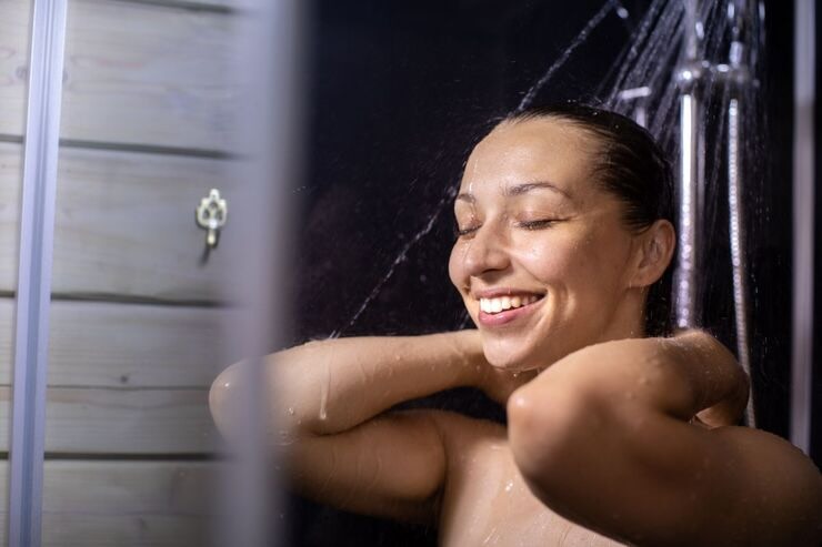 Ragazza sorridente sotto getto d'acqua della doccia
