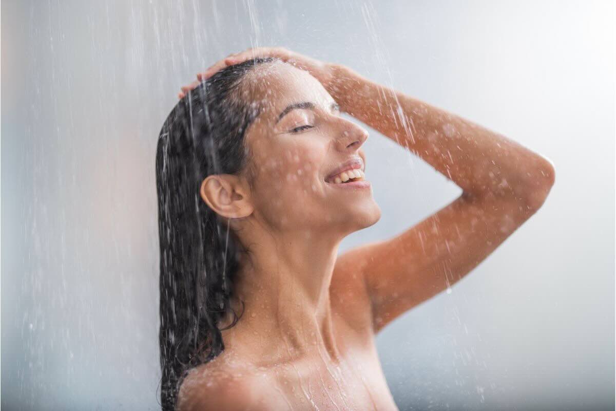 Ragazza sorridente sotto getto d'acqua della doccia