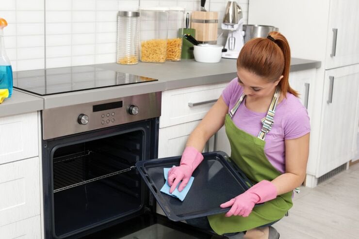 Donna vicino il forno pulisce la teglia con un panno azzurro