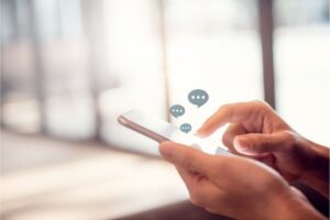 Mano che digitano su schermo smartphone, nuvolette messaggio con puntini