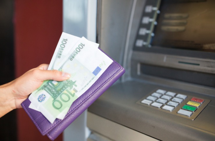 sportello bancomat e donna con in mano il portafoglio e due banconote da 100 euro
