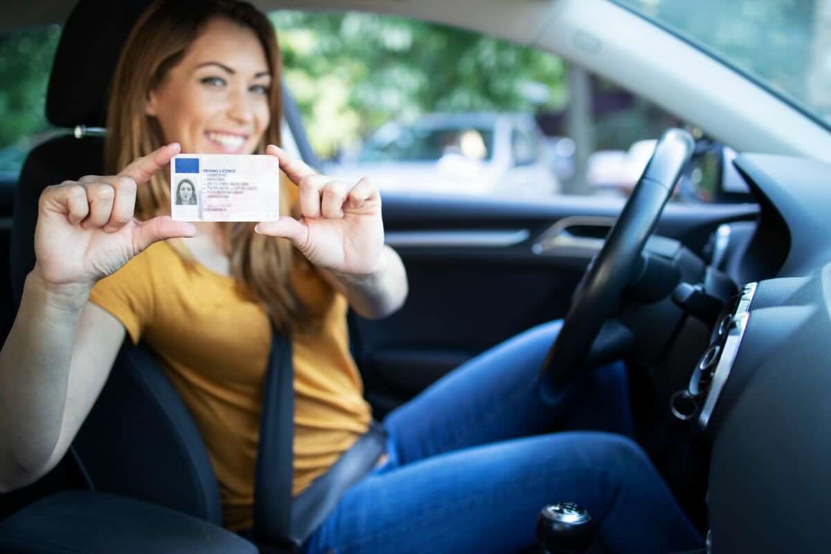 Ragazza in auto con cintura di sicurezza, sorridente mostra patente