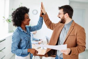 uomo e donna in ufficio che sorridono e battono il 5 con le mani
