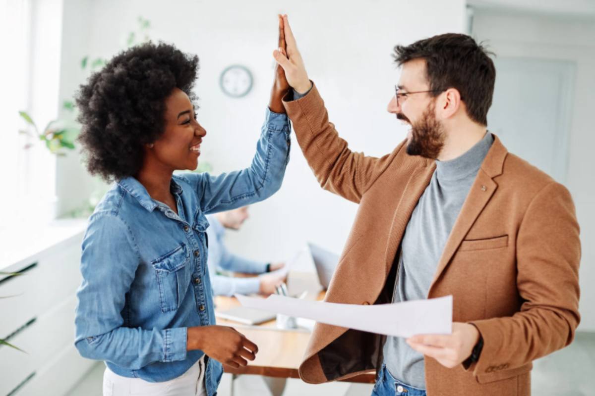 uomo e donna in ufficio che sorridono e battono il 5 con le mani