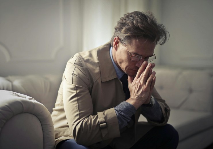 uomo seduto sul divano con le mani congiunte davanti al viso