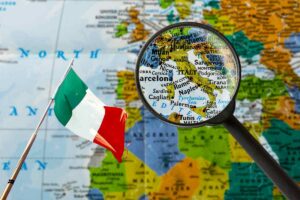 cartina geografica con una lente di ingrandimento che ingrandisce l'Italia e sulla sinistra una bandiera Italiana