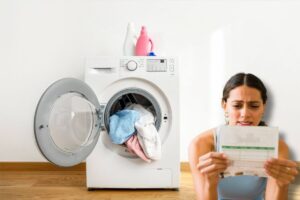 Sul fondo lavatrice aperta con vestiti e davanti ragazza legge bolletta