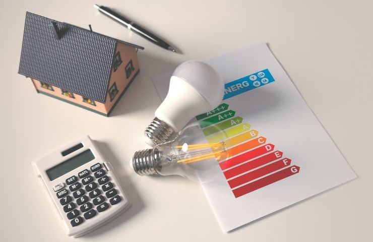 una piccola casa con delle lampadine ed un foglio vicino con le categorie della classe energetica