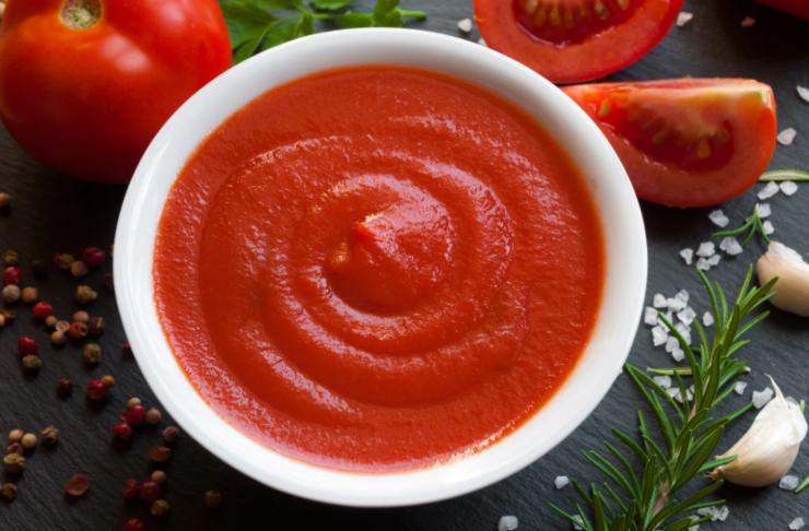 ciotola con dentro della passata di pomodoro e attorno aglio e pomodori