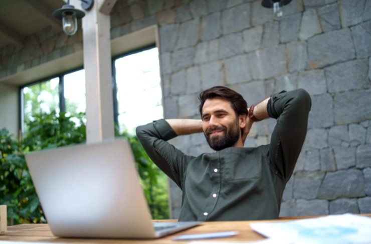uomo che sorride con le mani dietro alla testa seduto davanti al computer