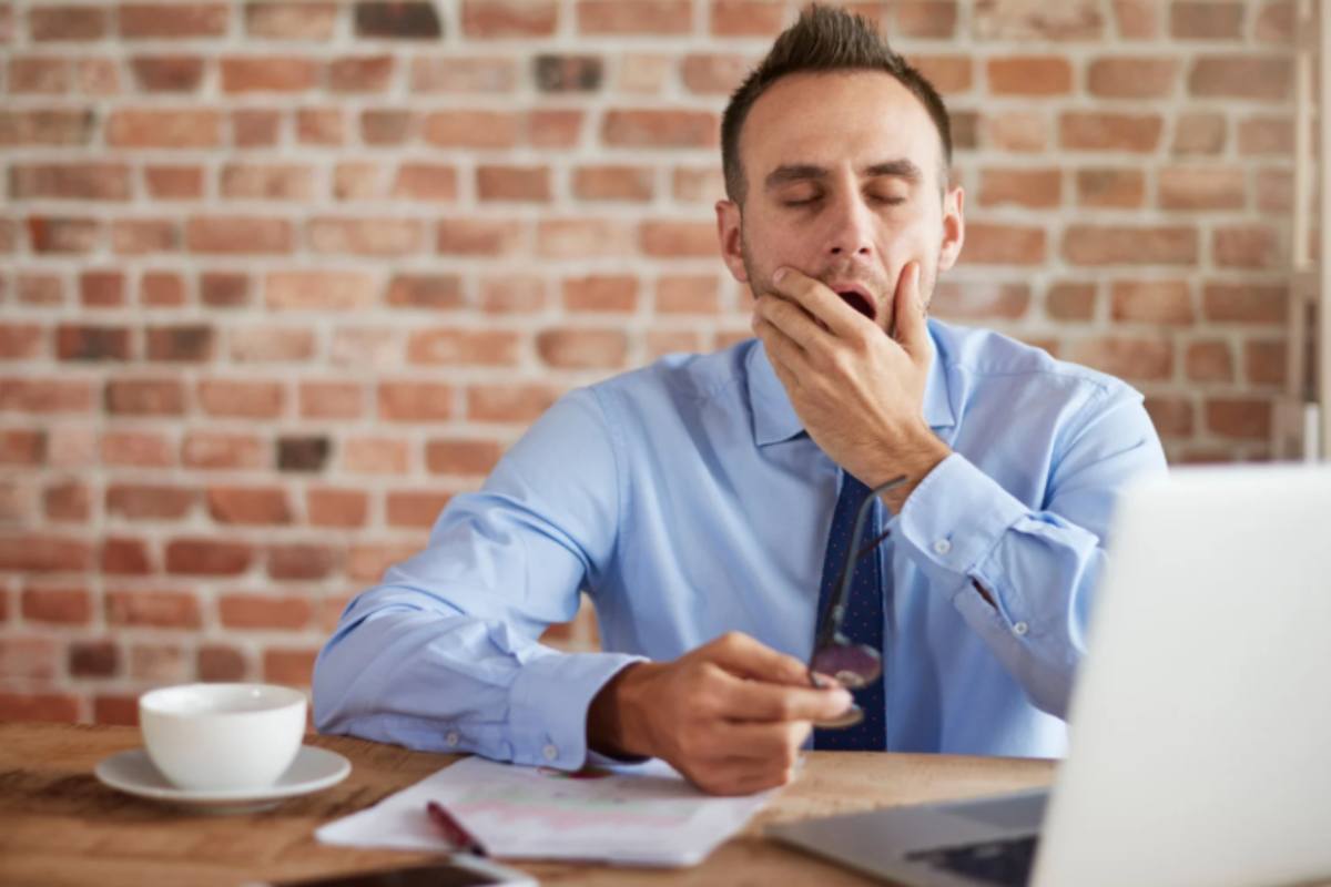 uomo che sbadiglia con gli occhi chiusi seduto di fronte al computer