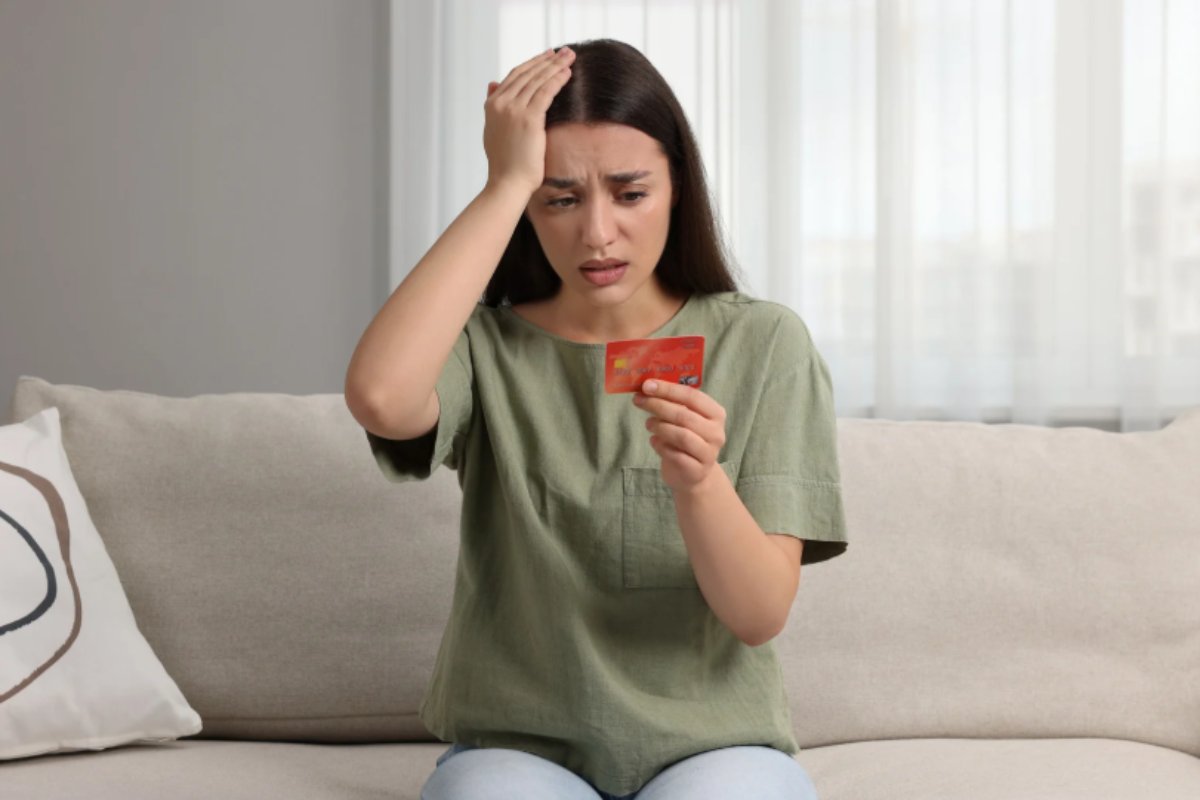 donna seduta sul divano con una mano in testa e nell'altra mano una carta di credito