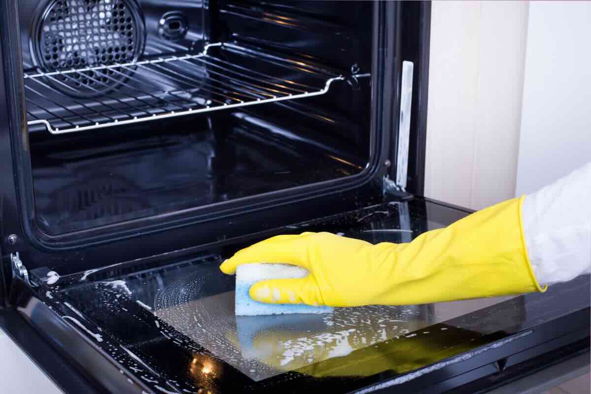 mano con guanto e spugna per pulire il forno