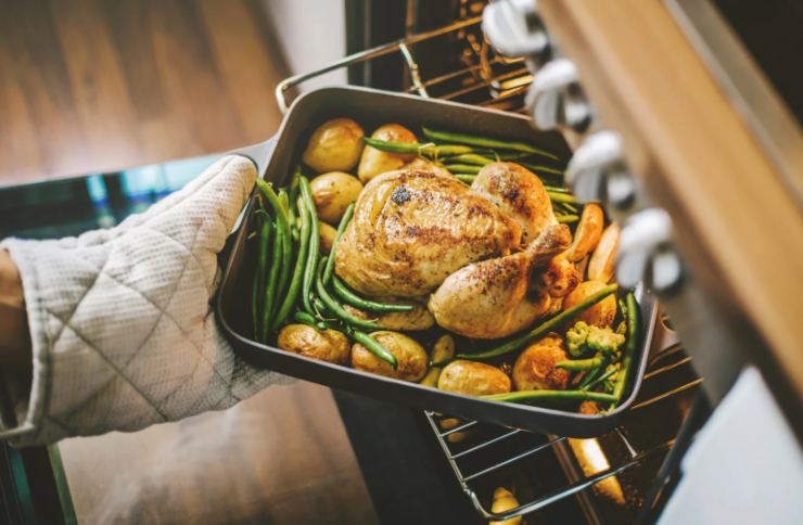 donna che prende una teglia dal forno con dentro pollo arrosto e verdure