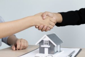 due persone che si stringono la mano e dietro una casetta in miniatura