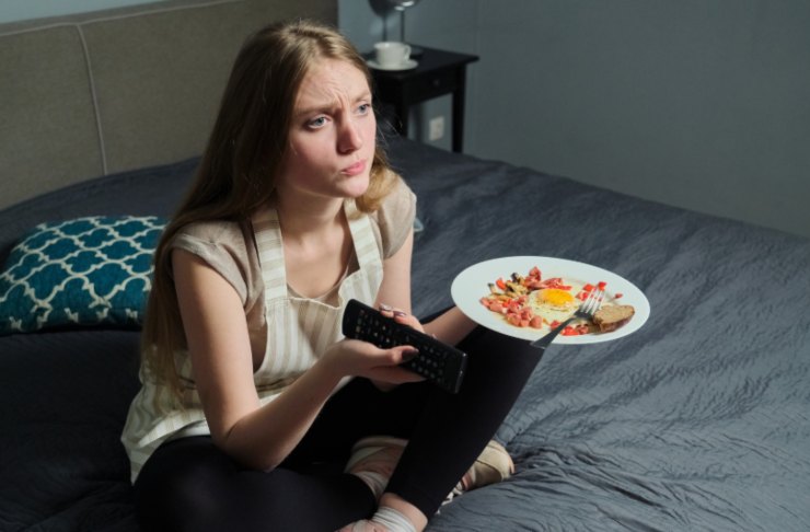donna seduta per terra che mangia mentre guarda la tv