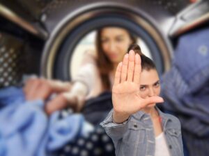 donna che mette bucato in lavatrice e un'altra che fa stop con le mani