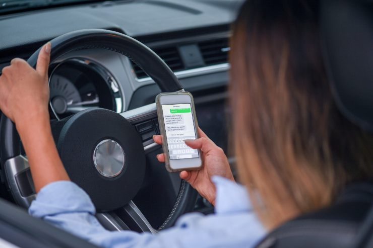 donna che usa il cellulare per scrivere un messaggio mentre è alla guida