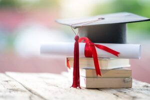 sfonfo sfocato con in primo piano dei libri una pergamena arrotolata ed un cappello di laurea messi uno sopra l'altro