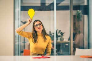 donna seduta ad un tavolo con una lampadina sopra alla testa