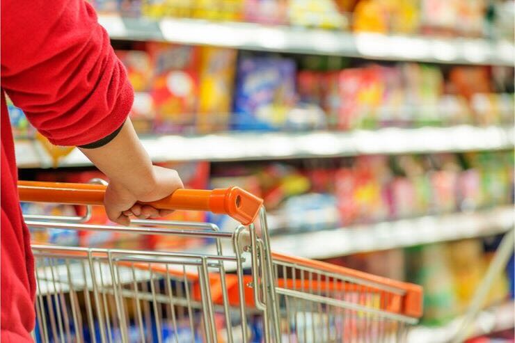 Mani tengono carrello fra scaffali supermercato