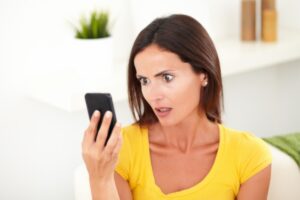 donna con espressione scioccata con in mano il cellulare