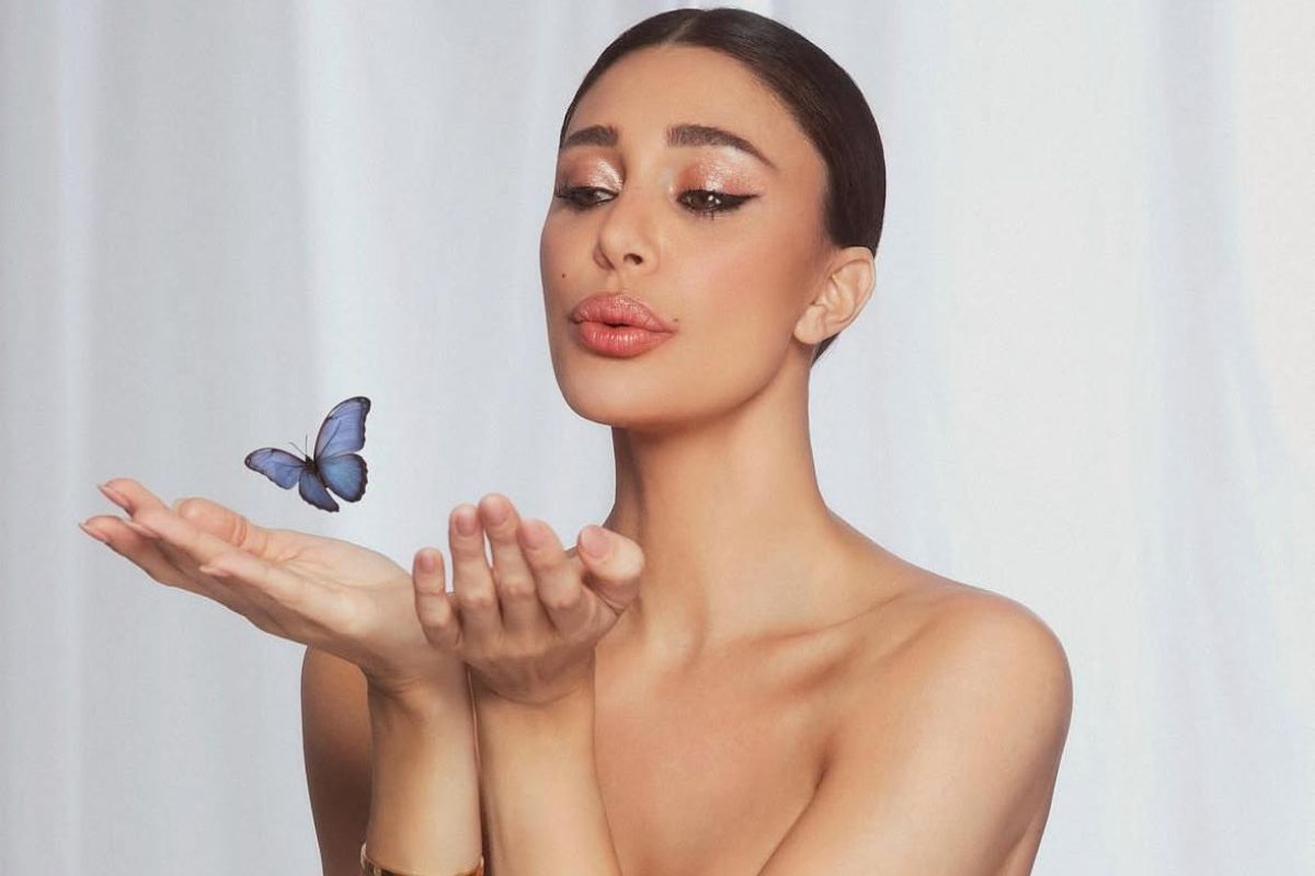 una foto di Belen in posa svestita con una farfalla tra le mani