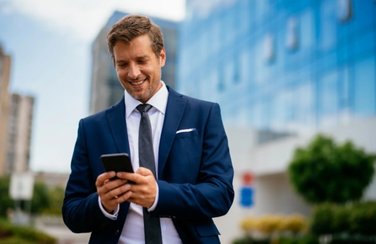 uomo in giacca e cravatta che sorride con in mano il cellulare