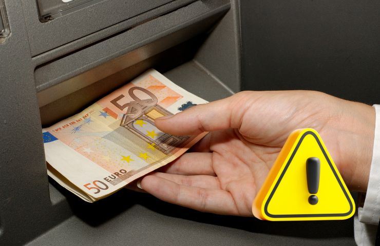 una persona preleva dei soldi in un bancomat e il simbolo attenzione