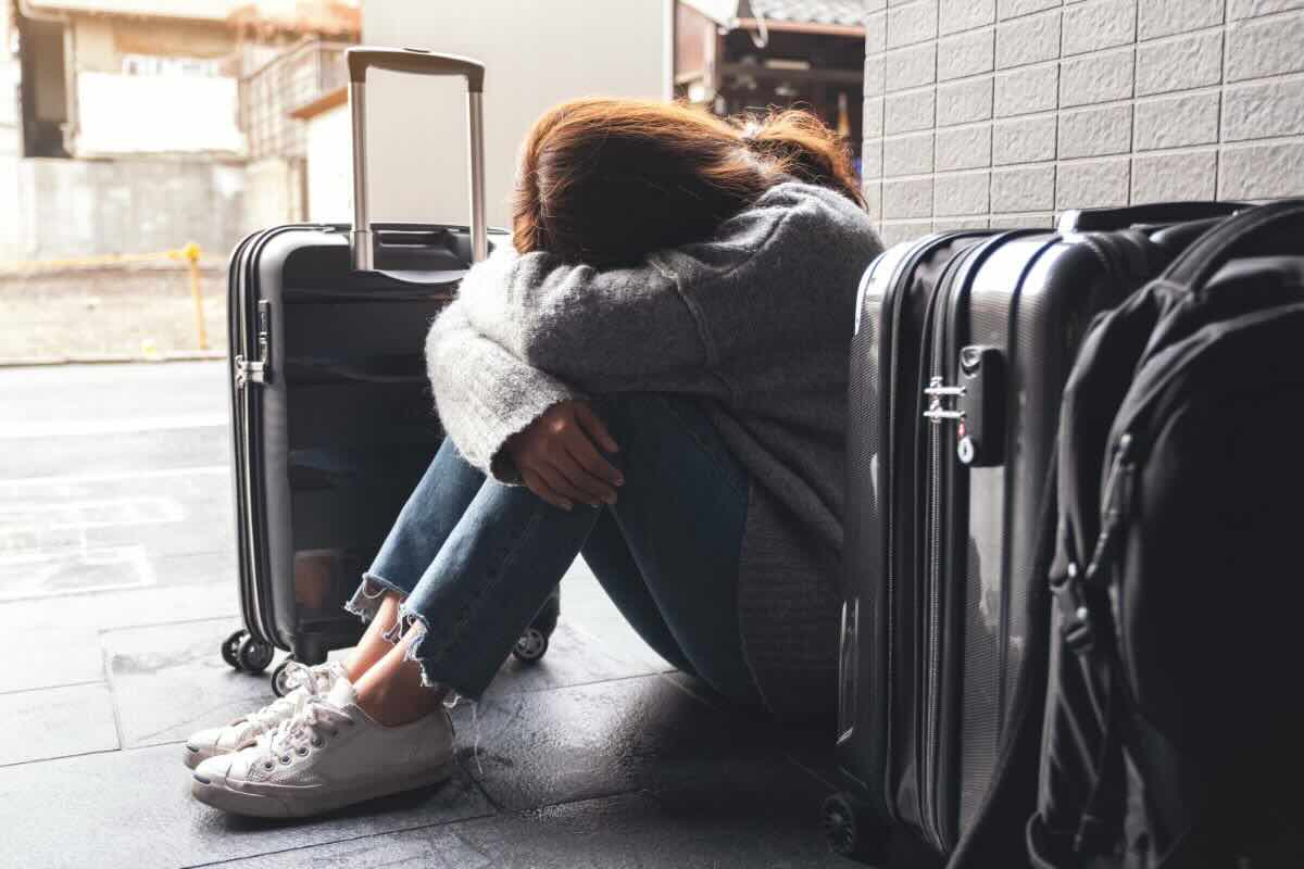 Ragazza seduta con viso sulle gambe, attorno a lei bagagli