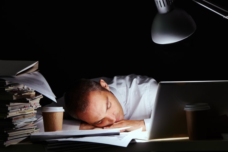 Un dipendente che si è addormentato sulla scrivania con dei documenti di lavoro sopra