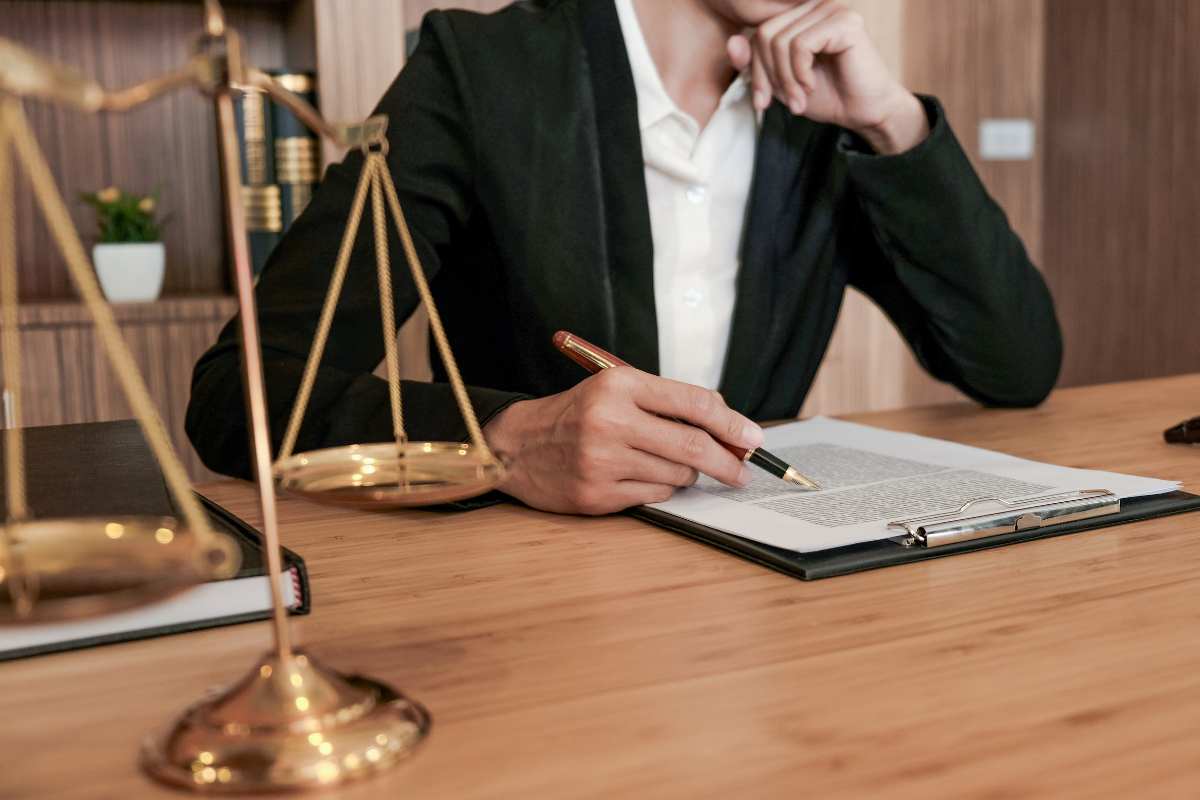 avvocato che scrive su un foglio ed in primo piano una bilancia come simbolo di giustizia